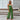 Beige sleeveless jumpsuit with a tie-waist, styled elegantly for casual summer wear, displayed on a mannequin with a flowerpot and green plant nearby, showcasing its fashionable design.