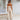 A beige sleeveless jumpsuit featuring a tie-waist design, suitable for elegant casual summer wear. The jumpsuit highlights areas such as the neckline, waist, and thighs, and is showcased against a wooden floor background.