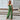 Beige tie-waist sleeveless jumpsuit displayed on a person, showcasing its elegant and casual summer style, with a focus on the waist and thigh areas. The background includes a flowerpot with a houseplant, enhancing the casual and stylish atmosphere.