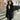Black faux fur hooded vest worn by a woman, showcasing an elegant winter fashion style. The vest features a hood and sleeveless design, highlighting the shoulder and neck area. The outfit is complemented by a stylish hairstyle.