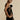 A woman wearing a black floral sheer one-shoulder evening dress, showcasing intricate floral patterns and elegant design, with her hair styled neatly, captured in flash photography.