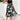 Woman wearing a black floral sleeveless midi dress, showcasing elegant summer formal attire, standing with hands by her sides and wearing black footwear.