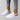 Black leopard print women's stylish comfortable sneakers shown on a white and grey textile background with a plant in the vicinity.