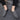 Men's black textured leather slip-on loafers with zipper, shown on a person wearing blue denim jeans, standing on a grey floor surface.