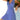 A smiling woman wearing a blue and white geometric V-neck sleeveless A-line summer dress.