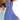 A woman wearing a blue and white geometric V-neck sleeveless A-line summer dress, smiling with her hands by her side.