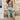 A woman wearing a bohemian floral wide-leg jumpsuit, styled for a summer beach outing, standing with her hands on her hips. She is accessorized with sunglasses and showcasing the flowy design of the jumpsuit that features a relaxed fit around the waist and wide legs.