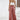 Woman wearing a white lace top and rust palazzo pants, accessorized with a straw hat, standing in a relaxed pose.