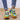Colorful rainbow sneakers featuring a vibrant multicolor pattern with shades of electric blue, yellow, and magenta, worn on a human foot against a denim background.