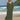 Elegant green V-neck caftan worn by a person standing on a beach with a clear sky and ocean in the background. The lightweight, flowy dress features short sleeves and a cinched waist.