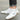Men's white high-top designer sneakers with grey and electric blue accents, showcasing an urban streetwear style, worn by a model with visible lower legs in a sporty and fashionable setting.