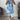 A woman wearing a sleeveless summer tunic top with a floral print design in shades of blue and white, featuring a round neckline and a relaxed fit at the waist.