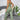 Woman wearing a green ribbed lace trim jumpsuit standing in a cozy indoor setting with plants in the background.