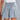 Woman wearing a green smocked summer skirt with an elastic waist and ruffles, paired with a white top.