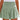 Woman wearing a green smocked summer skirt with elastic waist and ruffles, standing outdoors.