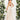 Ivory backless maxi dress with crossover straps, featuring pockets and a flowing design, worn by a model standing amidst greenery, highlighting the elegant neckline and sleeveless cut.