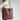 A large caramel brown handmade leather tote designed for women, featuring a spacious interior suitable for work essentials. The bag includes a shoulder strap for easy carrying and showcases a hobo style for a fashionable appearance.