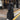Woman in an oversized, full-length black puffer coat with quilted design, standing on an asphalt road.