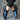 Luxury black leather men's formal shoes with a designer checkered pattern, worn by a person dressed in casual denim clothing, highlighting the sleek and elegant footwear against the lower body.