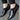 Black leather men's formal shoes with a designer checkered pattern, displayed on a model's feet.