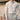 Luxury men's beige knit polo sweater paired with vintage pleated trousers, showcasing elegant outerwear with a collared neckline and long sleeves. The ensemble highlights a sophisticated style with attention to the waist and elbow details.