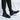 Men's black leather Chelsea boots, showcasing a formal slip-on design, worn on a human leg, emphasizing their ankle-height style and sleek appearance.