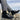Men's black lightweight sneakers, designed for breathability, non-slip, and shock absorption, worn by a person walking outdoors, partially visible with jeans against a natural background.