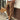 Men's slim fit brown pleated trousers displayed on a model. The trousers have a lightweight design suitable for urban fashion. The model is wearing a dress shirt tucked into the trousers, demonstrating a stylish and formal appearance.