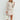 Luxury women's workwear featuring a multicolor tweed jacket and skirt suit with white accents, long sleeves, and a collar. Model showcases the suit with a stylish handbag.