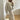 A woman wearing an oversized grey sweater with long sleeves and a comfortable fit, paired with a gold chain bag. She is standing on a floor, accessorized with stylish eyewear, capturing a trendy and casual fashion look.