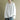 A woman wearing an oversized white sweater made of a casual cotton blend, paired with a dress shirt underneath. The sweater features long sleeves and the image focuses on the torso area up to the waist.