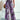 A pair of wide-leg palazzo pants featuring a paisley print in shades of purple, pink, and violet, designed for a bohemian summer style. The pants have a comfortable fit around the waist and flow elegantly down to the ankles. Shown in the Viola color variant and size 2XL.
