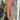 A woman wearing a peach mid-length spring dress, standing with a relaxed posture and smiling. The dress is casual yet elegant, made from lightweight fabric. She is accessorized with sunglasses, complemented by her surroundings which include a houseplant in a flowerpot, adding a touch of nature and warmth to the scene.