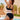 Plus size woman wearing a black crochet halter bikini set with high-waisted bottoms, standing near water under a cloudy sky.