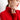 A woman wearing a red ribbed turtleneck sweater in size 2XL, accessorized with gold pearl hoop earrings. Her hair is styled neatly, and she has makeup on, including lipstick and eye makeup.