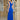 A woman wearing a royal blue V-neck bodycon evening gown with a backless design, showcasing the elegant fit around the shoulders and waist, standing near a window.