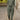 A woman standing wearing a green 3XL rust linen jumpsuit set featuring a sleeveless design, eco-friendly fabric, and a comfortable fit suitable for summer fashion.