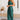 A woman wearing a rust satin midi slip dress with a backless design and tie-back detail, standing with a smile. Her arms are visible, and the dress is elegant, showcasing a silky texture. The setting suggests a formal occasion.