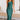 A green satin midi slip dress in a sheath silhouette, featuring a backless design with tie-back detailing. The dress is modeled in a size XL, showcasing its elegant and form-fitting style.