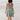 Sea green smocked backless tiered women's summer dress worn by a woman near water, with visible shoulders and arms, highlighting the dress's flowing one-piece design.
