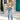 A person wearing a blue and white star pattern crewneck sweater paired with jeans, standing in front of a door. The sweater features long sleeves and a casual knit design.