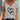 Woman wearing stylish V-neck gray graphic tee with heart print, paired with jeans, standing outdoors.