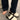 Stylish women's black platform orthopedic sandals with ankle strap being worn by a model dressed in denim trousers, standing on a grey floor.