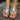 A pair of Tribal Pattern Women's Sandals in black, featuring a boho chic design, worn on a woman's feet with a visible patterned design and blue accents. The image captures the sandals against a natural backdrop with greenery.