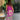 Tropical maxi dress with a vibrant purple and green palm design, featuring loose sleeves and a flowing silhouette. The dress is being worn outdoors near a fence, surrounded by greenery and grass, showcasing a colorful pattern with tints and shades of magenta.