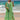 Woman wearing a Tropical Print Green Beach Kaftan, standing near the water with a clear blue sky in the background.