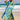 A woman wearing a tropical print green beach kaftan dress with V-neck, standing by the water under a clear sky.