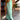 Turquoise tie-dye maxi dress with sleeveless design, ideal for beachwear, displayed on a model in a natural outdoor setting with plants and wooden flooring.
