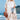 A woman wearing a white boho kimono with embroidered floral patterns, standing near water, showcasing summer beachwear.