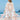 White boho kimono with embroidered floral patterns, luxury summer beachwear, worn by a woman standing on a beach near the water under a clear blue sky.